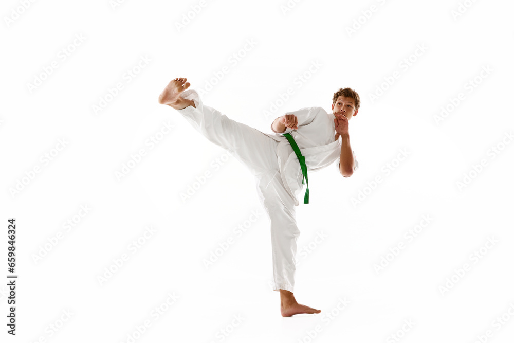 Combat sport athlete, young man in white kimono, practicing karate isolated on white studio background. Concept of martial arts, combat sport, energy, strength, health. Ad