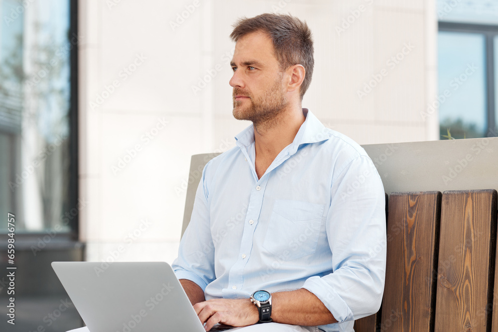 Businessman sitting on a bench with a laptop and solving business issues Businessman sitting on a bench with a laptop and solving business issues