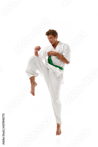 Combat sport athlete, young man in white kimono, practicing karate isolated on white studio background. Concept of martial arts, combat sport, energy, strength, health. Ad