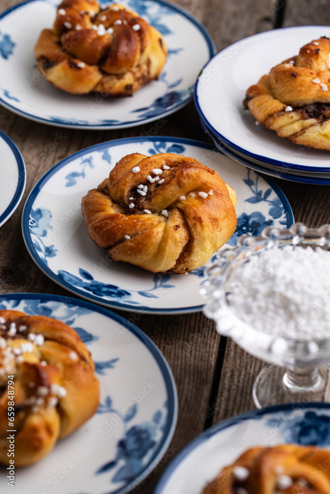 Homemade traditional Swedish cinnamon buns (swirls) on separate white and blue porcelain plates on wooden table. Homemade traditional Swedish cinnamon buns (swirls) on separate white and blue porcelain plates on wooden table.