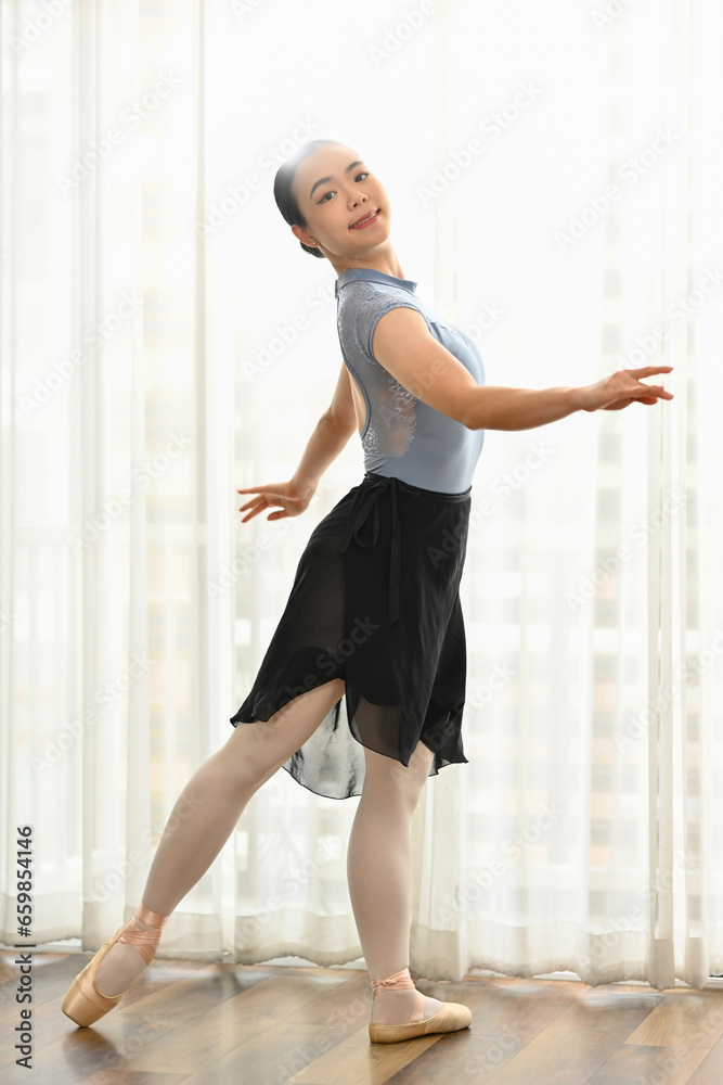 Portrait of elegant female dancer in pointe shoes practicing ballet positions near large window Portrait of elegant female dancer in pointe shoes practicing ballet positions near large window