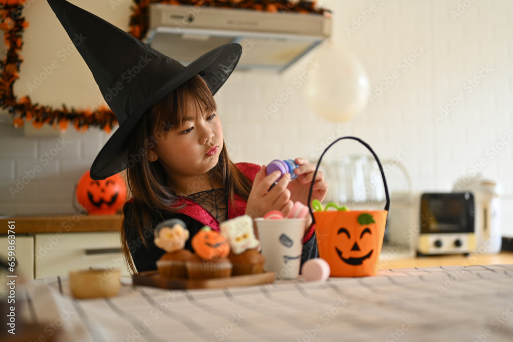 Adorable little girl decorating Halloween cupcakes with different monsters, pumpkins and ghosts