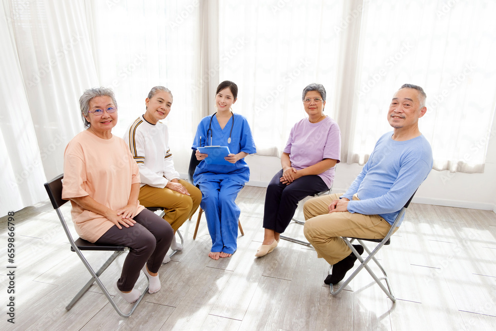 The caregiver therapist sits with a group of Asian senior people looks at the camera in a circle to check physical and mental health in a group elderly therapy session. The nursing home facilitates The caregiver therapist sits with a group of Asian senior people looks at the camera in a circle to check physical and mental health in a group elderly therapy session. The nursing home facilitates