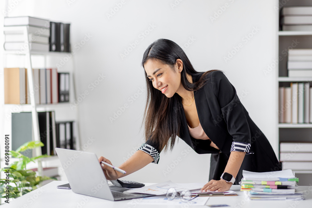 Asian Businesswoman Using laptop computer and working at office with calculator document on desk, doing planning analyzing the financial report, business plan investment, finance analysis concept.
