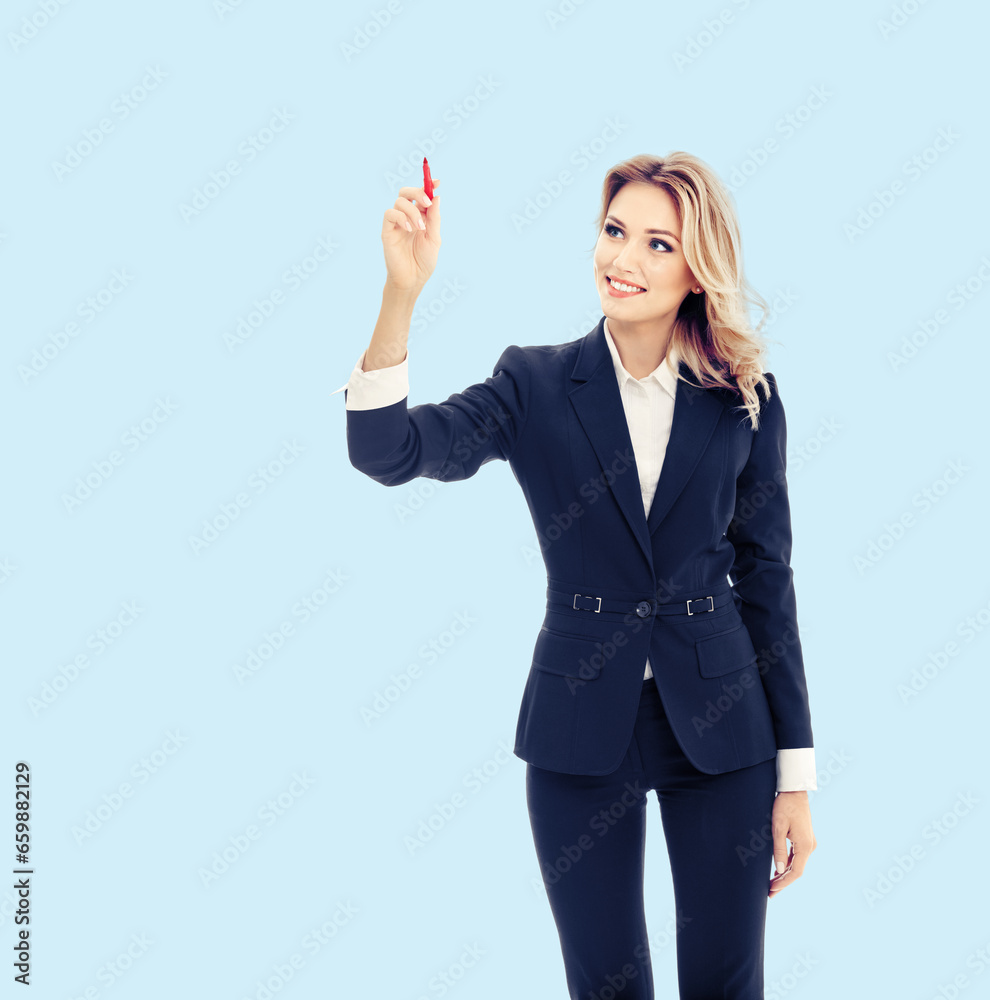 Smiling young businesswoman in dark blue confident suit, writing or drawing something on screen or transparent glass, by marker, isolated over bright sky blue background. Smiling young businesswoman in dark blue confident suit, writing or drawing something on screen or transparent glass, by marker, isolated over bright sky blue background.