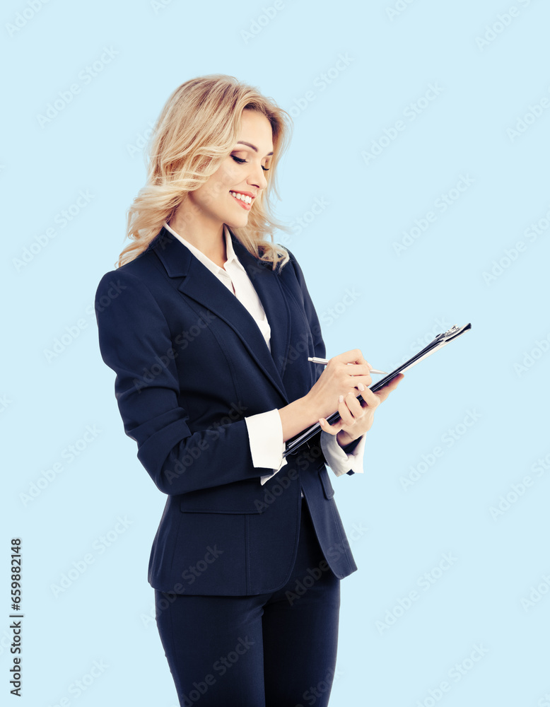 Young beautiful businesswoman in dark confident suit, with clipboard writing, isolated bright sky blue color background. Business studio concept image. Copy space for some text. Young beautiful businesswoman in dark confident suit, with clipboard writing, isolated bright sky blue color background. Business studio concept image. Copy space for some text.