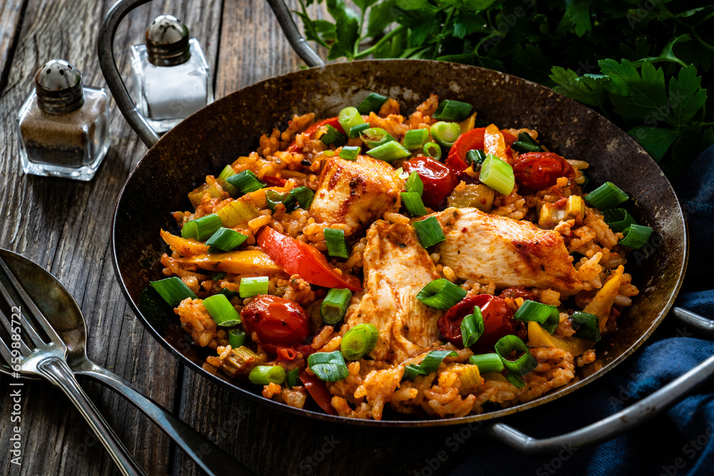 Jambalaya one pot dish - fried chicken breasts with white rice, tomatoes, bell pepper and celery on wooden table

