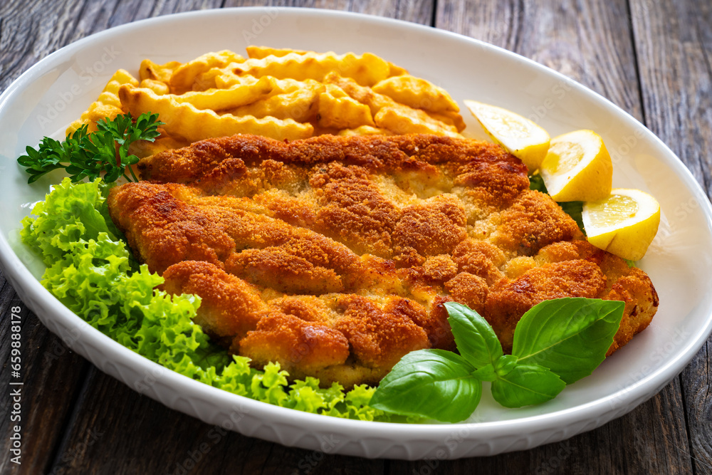 Crispy breaded seared chicken cutlet with French fries, lemon and fresh vegetables on wooden table
Crispy breaded seared chicken cutlet with French fries, lemon and fresh vegetables on wooden table