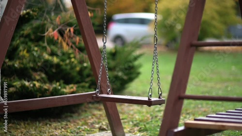 Empty wooden kids' swing moving in slow motion on playground or backyard