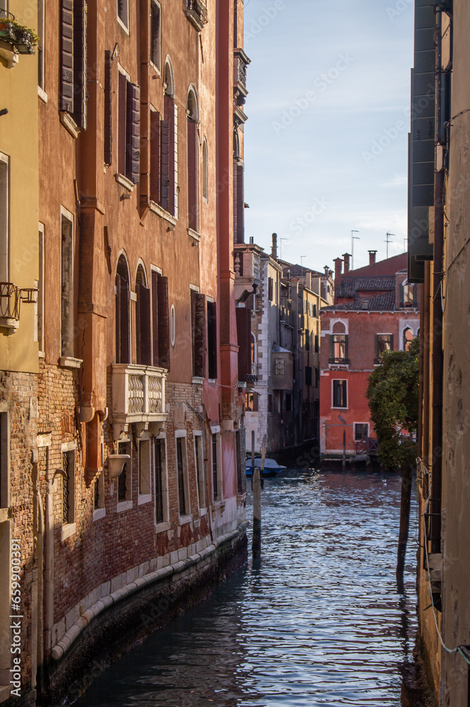 Narrow canal. Venitian architecture, buildings, dark water in the canal, reflection on the water, evening light. Crumbling buildings. Dark shadows, sky in the background. Venice during covid-19.