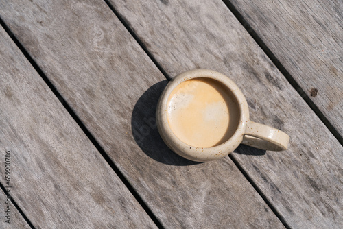Coffee cup with coffee on wooden surface in summer sun light top view. Clay or ceramic mug with blurry background and copy space. Beautiful summer coffee vibes morning relaxing. 