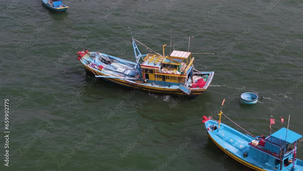 Vibrant yellow and blue fishing boat in vietnam drags round circular boat behind, aerial tracking Vibrant yellow and blue fishing boat in vietnam drags round circular boat behind, aerial tracking