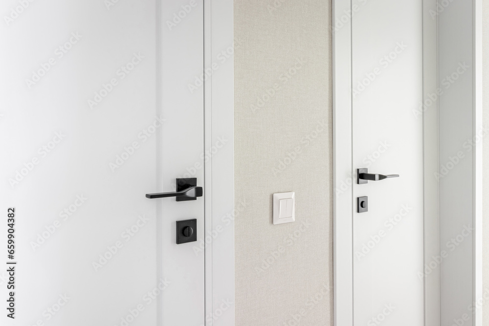 Modern black door handle on white wooden door in interior. Knob close-up elements Modern black door handle on white wooden door in interior. Knob close-up elements