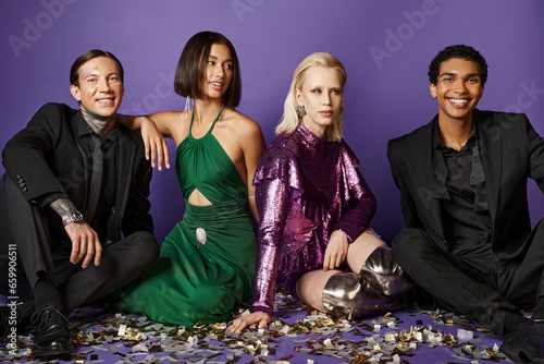 New Year 2024  interracial friends in party clothes sitting on festive confetti on purple backdrop