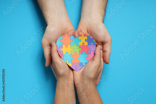 Heart made of puzzles in hands on blue background, top view