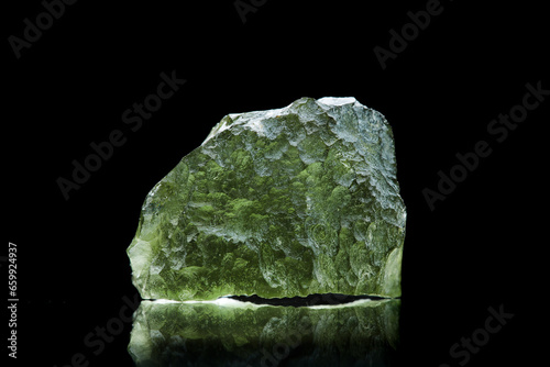 Moldavite stone isolated on black background. Close up macrophotograph of a green precious mineral from Czechia. Genuine natural tektite glass. photo