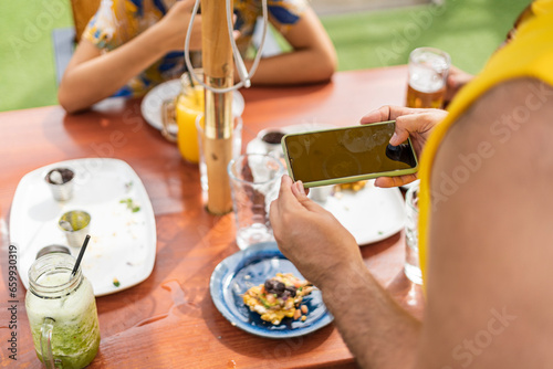 unrecognizable members of the lgbt community enjoying snacks and drinks at an outdoor restaurant and taking cell phone pictures of the food. photo
