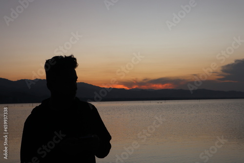 Silhouette of a young man standing by the lake enjoying the sunset. peaceful atmosphere in nature 