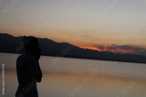 Silhouette of a young man standing by the lake enjoying the sunset. peaceful atmosphere in nature 