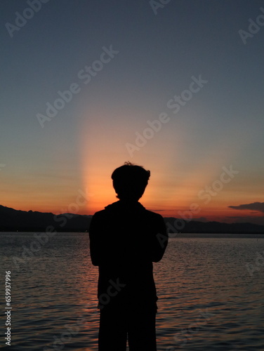 Silhouette of a young man standing by the lake enjoying the sunset. peaceful atmosphere in nature 