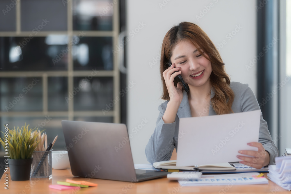 Portrait of a beautiful confident businesswoman using a laptop computer holding a mobile phone sitting in a modern office. Portrait of a beautiful confident businesswoman using a laptop computer holding a mobile phone sitting in a modern office.