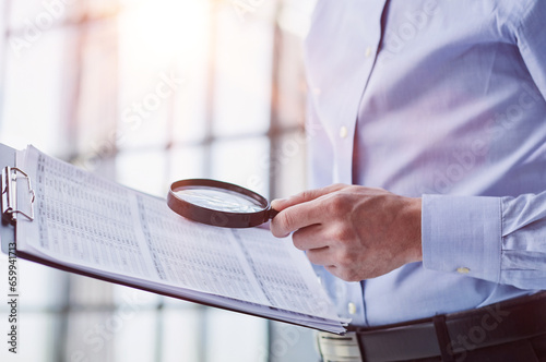 Businessman looking through a magnifying glass to documents