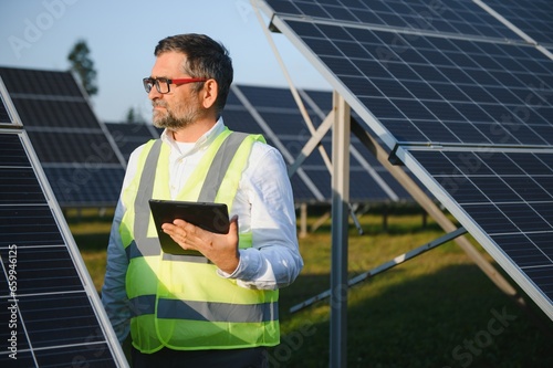 Elderly engineer is checking with tablet an operation of sun and cleanliness on field © Serhii