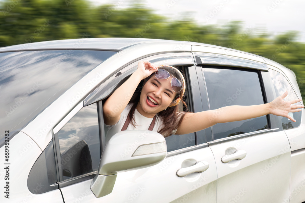 Happy young Asian woman enjoying a road trip and having fun waving at the air outside the car.