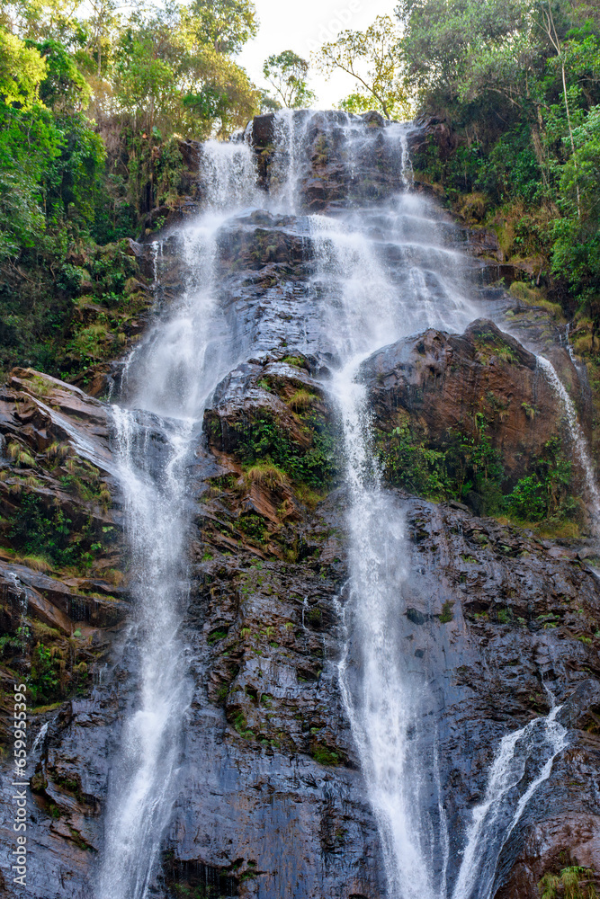Waters from a waterfall running down a large rock through rainforest vegetation in Minas Gerais, Brazil
