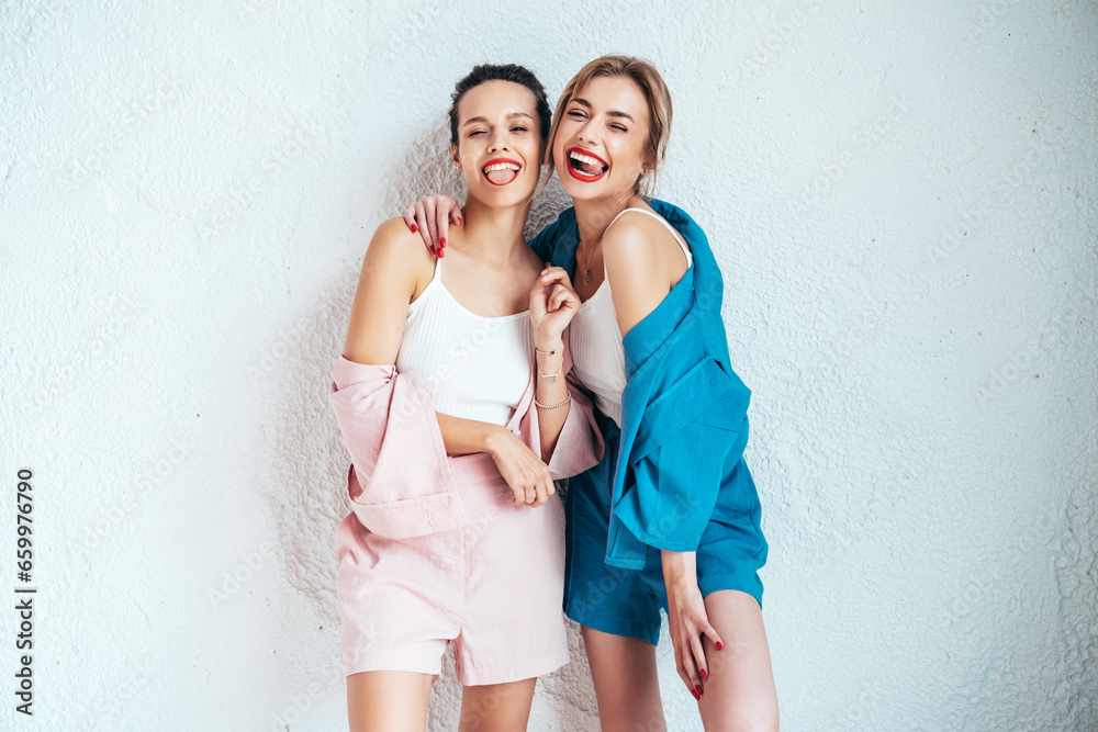 Two young beautiful smiling brunette hipster female in trendy summer clothes. Sexy carefree women posing near white wall in studio. Positive models having fun. Cheerful and happy. Going crazy Two young beautiful smiling brunette hipster female in trendy summer clothes. Sexy carefree women posing near white wall in studio. Positive models having fun. Cheerful and happy. Going crazy