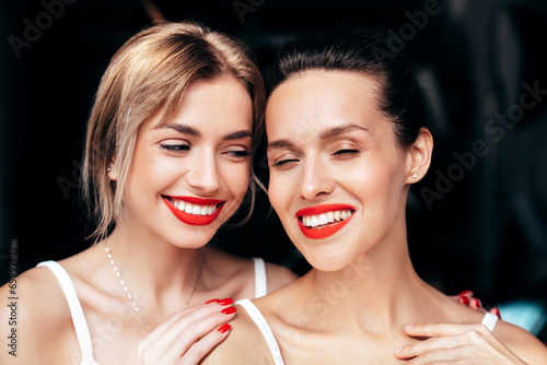 Closeup portrait of two young beautiful smiling brunette female with glamour evening makeup. Sexy women with healthy glowing face skin. Hot models with red lips posing over dark background