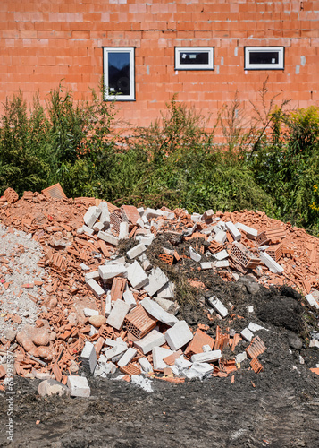 Heap of construction debris - broken pieces of bricks and concrete blocks, new building constructed in background