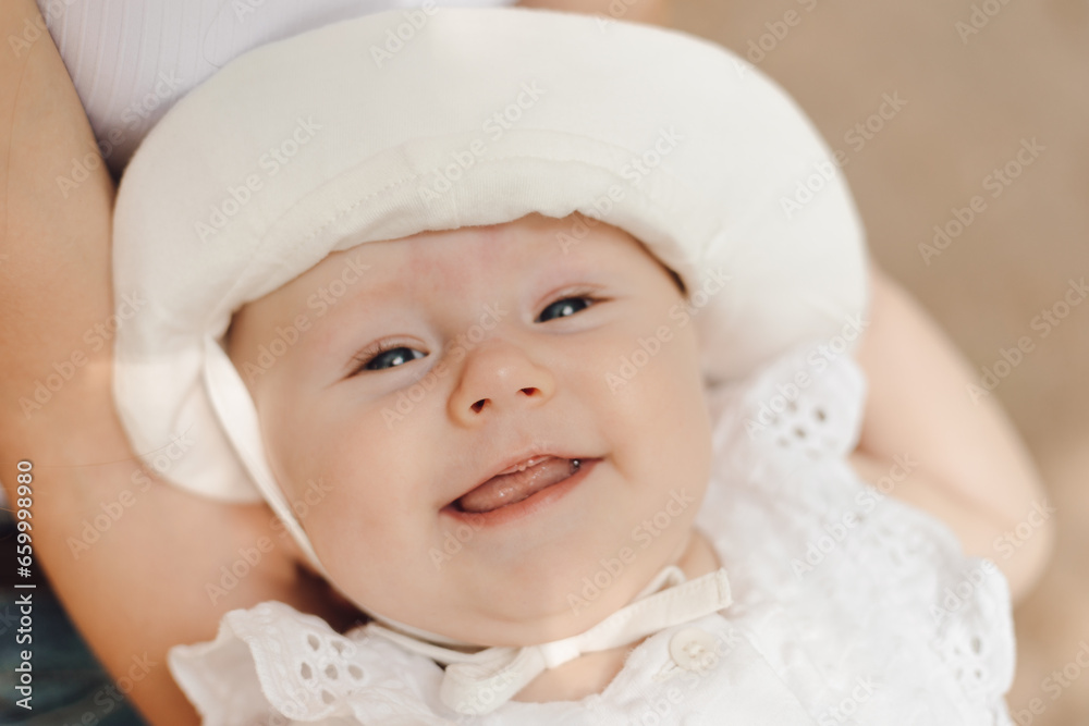 Close-up portrait of smiling toothless newborn girl in hat, held in arms of unrecognizable mother. Close-up portrait of smiling toothless newborn girl in hat, held in arms of unrecognizable mother.