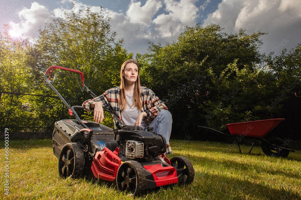 Female gardener working in autumn, cutting grass in backyard. Concept of gardening, work, nature. Housework, gardening and country life. Home garden grass cutting woman mowing with lawn mower.

