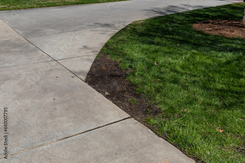Thick grass and dark soil beside the turn in a concrete sidewalk, cutting corners visual metaphor, creative copy space, horizontal aspect
