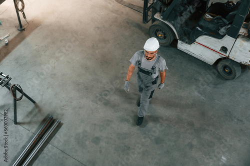 Near the forklift, top view. Young factory worker in grey uniform