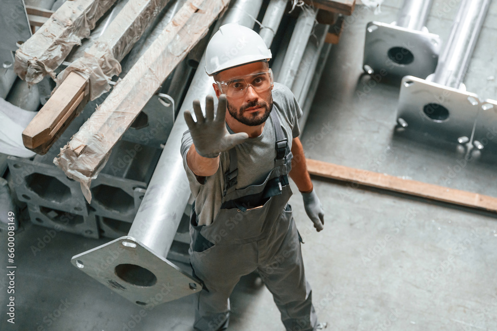 Top view. Making gesture by hands. Young factory worker in grey uniform
