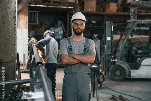 Another man is behind. Young factory worker in grey uniform