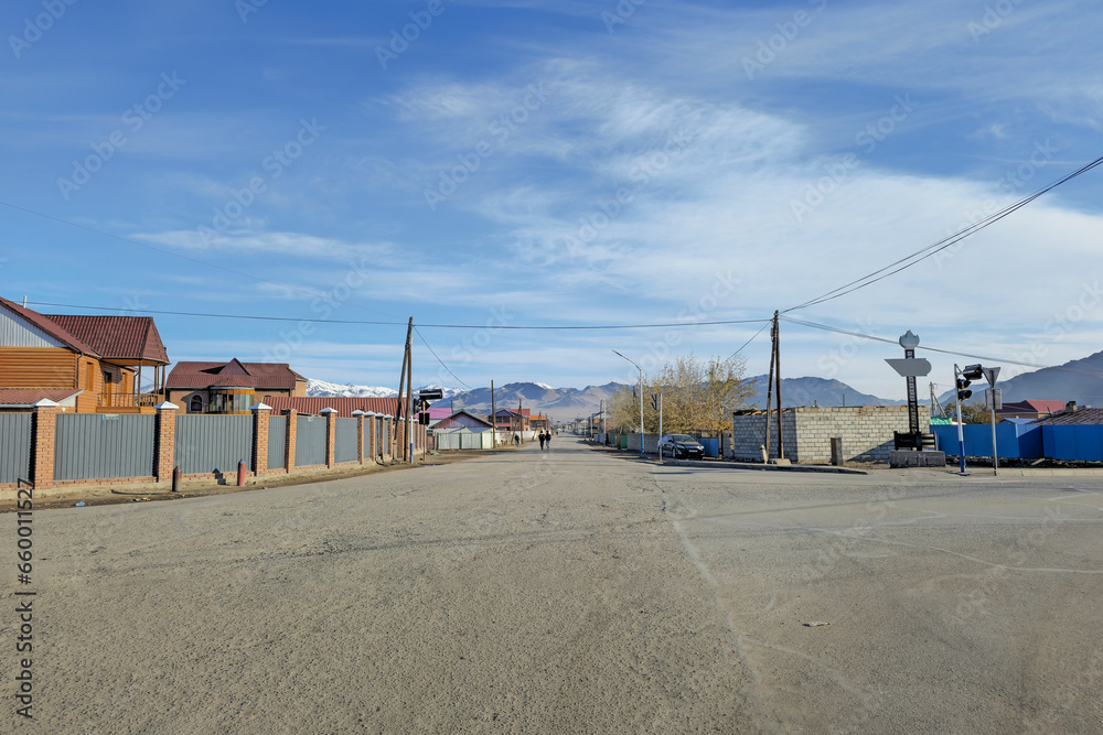 Northern Mongolia. City of Ulgiy. Houses of the street stretching into the distance to the mountains, Mongolian people on the street are busy with their worries.