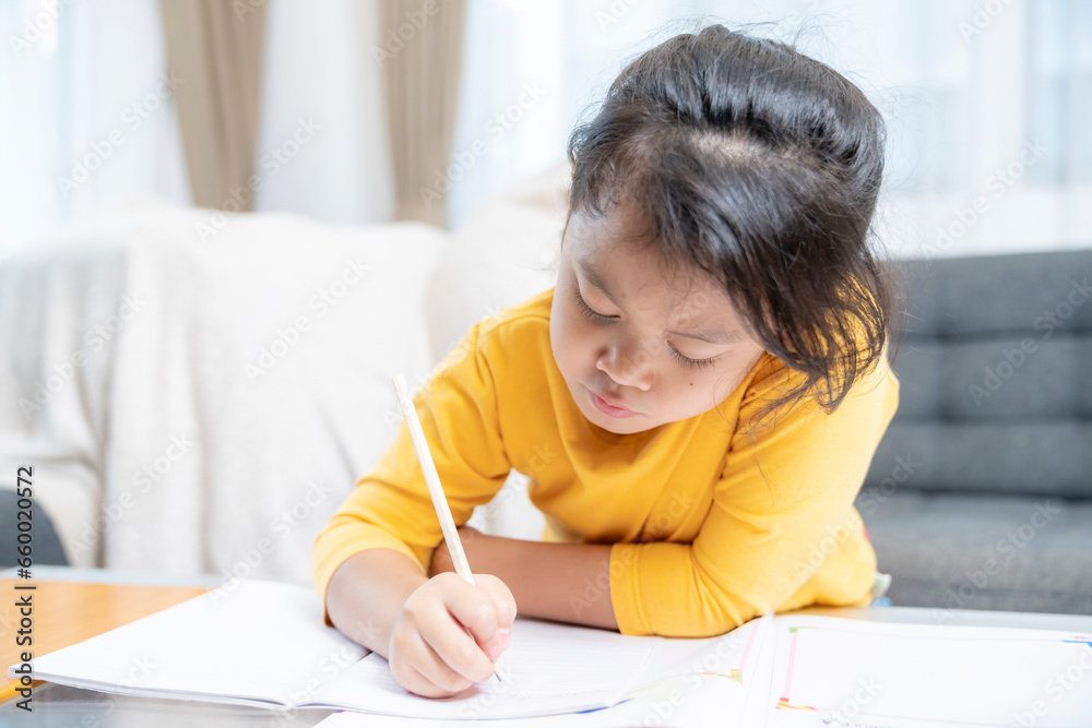 Cute little Asian child girl doing homework writing and reading at home Cute little Asian child girl doing homework writing and reading at home