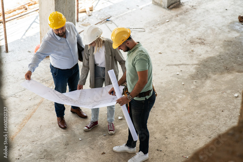 A female architect and construction manager work together on-site, discussing blueprints and coordinating to bring their project to life. Image taken from above.
