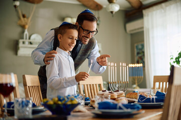 Happy Jewish father and son lighting menorah on Hanukkah.
