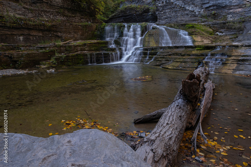 Waterfall in a deep gorge surrounded by forest trees during fall month. The water flows over a rocky cliffs into a deep pool. Long exposure, wide angle shot. Robert H Treman State Park, NY, USA. photo