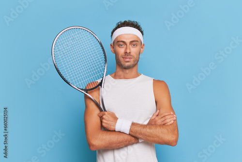  Young man stands with his arms crossed over his chest, pressing tennis racket to his chest, sports life concept, copy space © South House Studio