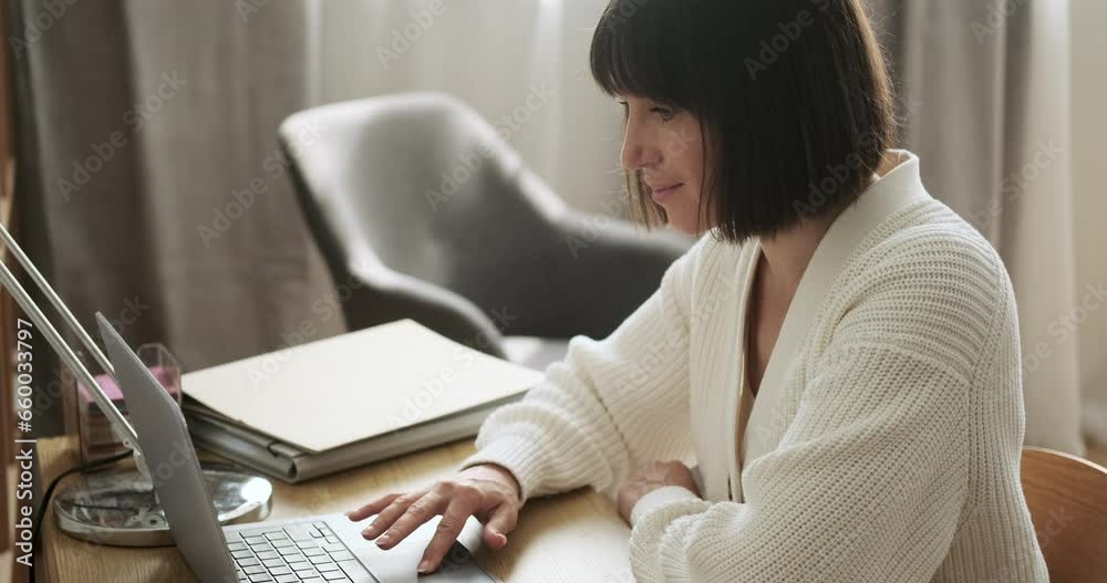 Cheerful Caucasian woman sits at a desk, typing on laptop with a warm ...