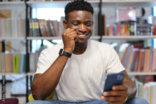 A happy young African American man, using a smartphone for online communication, combines technology and business.
