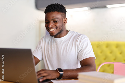 A confident African American businessman sits at a modern office desk, using a laptop, exuding professionalism.