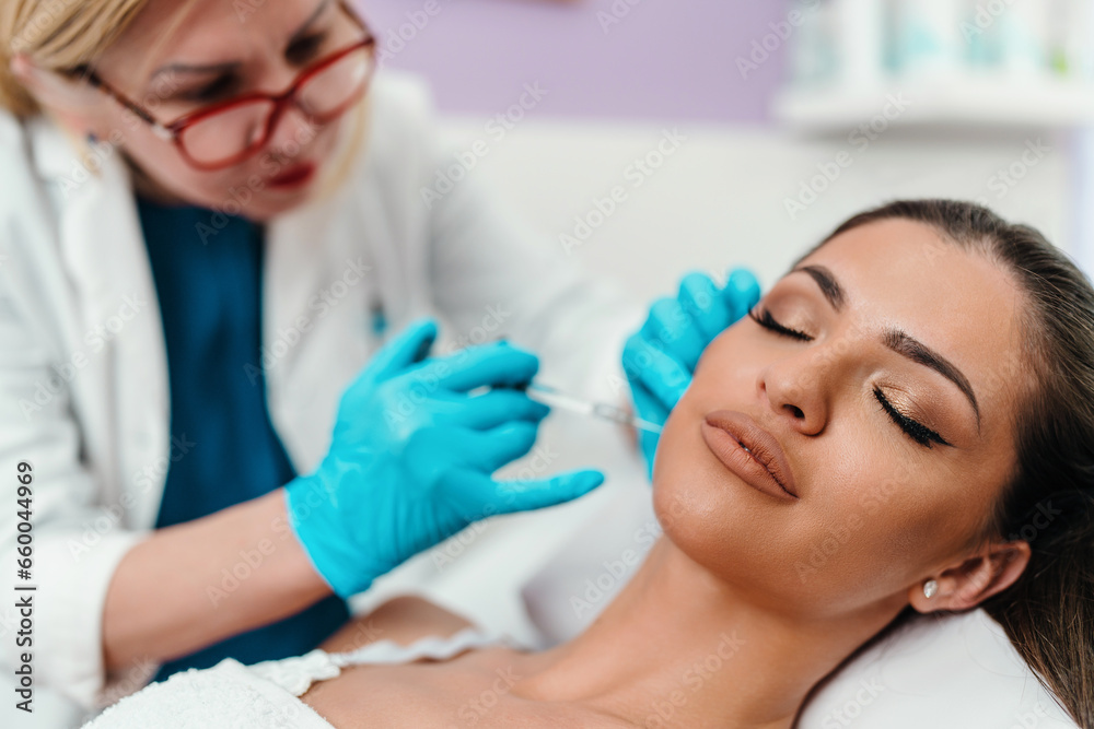 Beautician is contouring the woman's cheekbones with hyaluronic acid filler. Hyaluronic acid filler is injected by needle or cannula. Face contouring concept. Beautician is contouring the woman's cheekbones with hyaluronic acid filler. Hyaluronic acid filler is injected by needle or cannula. Face contouring concept.