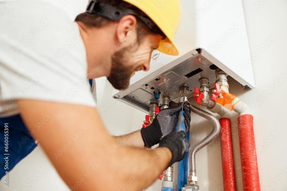 Closeup of plumber using screwdriver while fixing boiler or water heater, working on heating system in apartment