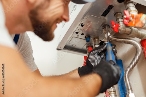 Closeup of plumber using screwdriver while installing new steel hot water central heating system in apartment